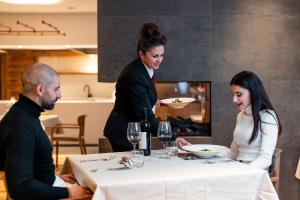 a woman sitting at a table with a woman holding a plate at Alpholiday Dolomiti Wellness & Family Hotel in Dimaro +29 photos