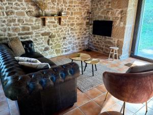 a living room with a leather couch and a tv at Le Gîte de Couturas in Saint-Hilaire-les-Courbes