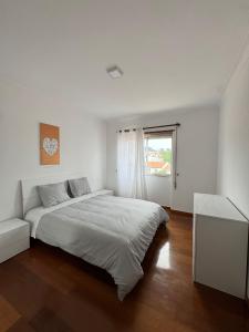 a white bedroom with a large bed and a window at Varanda do Coura in Caminha