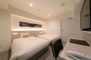 two beds in a room with a desk and a table at Vessel Inn Shinsaibashi in Osaka
