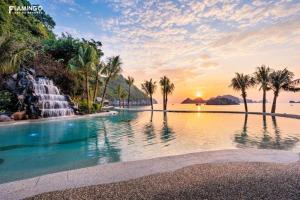 a pool with a waterfall and palm trees at sunset at Flamingo Cát Bà Sea Residence , Sky Villa Premier Ocean View King Bed in Hai Phong
