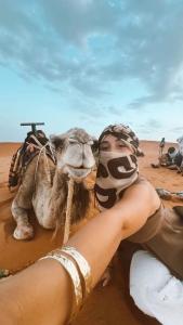 a woman laying on the sand with a camel at Merzouga Retreat Camp in Merzouga