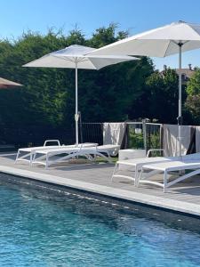 a group of white chairs and umbrellas next to a swimming pool at Villa Lilli Beta Bella Appartamento Verde comfort inclusivo design senza barriere in Neive