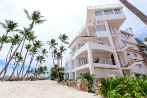 a white building on the beach with palm trees at DELUXE OCEAN view VILLAS & Apartments with POOL - PLAYA LOS CORALES, BBQ, SPA in Punta Cana