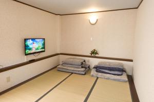 a room with two beds and a tv on a wall at Guest House Izumi in Izumi-Sano