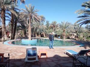 a man standing in front of a pool with palm trees at Maison Riad Tamarighte in Merzouga