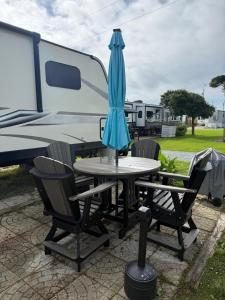 a table with an umbrella and chairs in front of an rv at RV by the Sea in North Topsail Beach