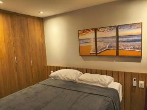 a bedroom with a bed with three paintings on the wall at Pé na areia, 3 suítes, terraço com piscina privativa in Camacari