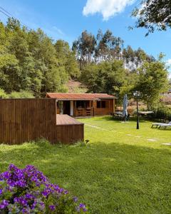 a log cabin in a yard with purple flowers at Ohana Gerês House in Ruivãis
