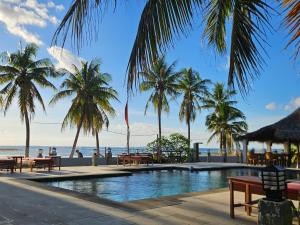 a swimming pool with palm trees and the ocean at Belar Reef Bungalows in Nembrala