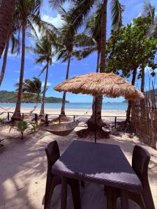 a table and chairs on a beach with a hammock at Beachfront Bungalows Bucana, El Nido in El Nido