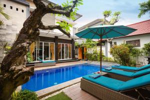 a pool with chairs and an umbrella next to a house at The Nakula Villas in Legian