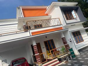 a white house with a red car parked in front of it at Coz Rooms in Varkala