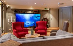 a living room with red chairs and a large screen tv at Villa Oleanna in Lysekloster