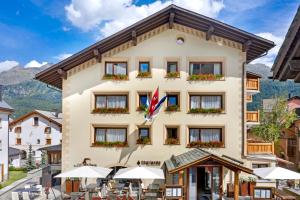 a hotel in the mountains with tables and umbrellas at Albana Hotel Silvaplana in Silvaplana