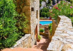 a stone wall next to a swimming pool with flowers at Amazing Sea View Terrace A with Pool 70m from the Beach in Baja Sardinia +11 photos