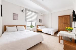 a white bedroom with two beds and a window at Chichi Inn Hotel CoTo in Đảo Cô Tô
