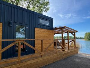 a black cabin with a wooden deck next to a lake at Ośrodek Dalpol in Prażmowo