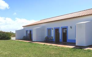 a white house with blue doors and chairs in a yard at O Monte da Estrada in Zambujeira do Mar