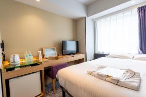a hotel room with a bed and a desk with a television at E Hotel Higashi Shinjuku in Tokyo