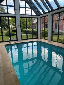 an indoor swimming pool with windows and blue water at Maison l'amitié in Ellezelles