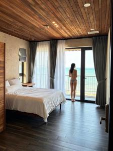 a woman in a hotel room with a bed and a window at Phuongvilla Đông Hải in Thôn Ðông Giang