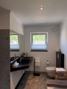 a bathroom with a sink and a toilet and two windows at Ferienwohnung Auszeit Langsur in Langsur