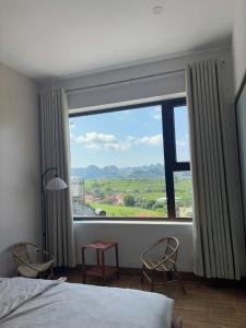 a bedroom with a large window with two chairs and a table at Lơ Mơ House in Làng Môn