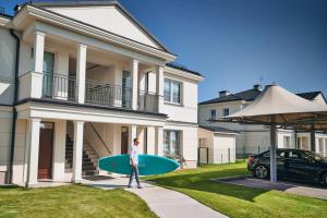 a person holding a surfboard in front of a house at Tesoro Dolce Vita Apartment in Pogórze +14 photos