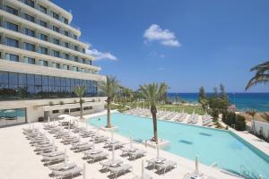 a large swimming pool with lounge chairs and the ocean at Sunrise Emerald in Protaras