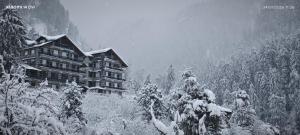 a large building on a snowy hill with trees at Manali Se - Your Home in the Pines in Jagatsukh
