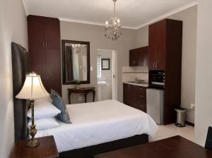 a bedroom with a white bed and a kitchen at Alimento Guest House in Upington