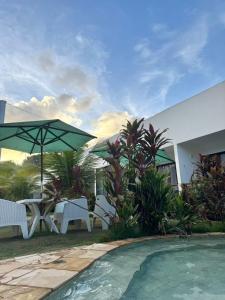 a pool with chairs and an umbrella next to a house at Mar Turquesa Eco Pousada in Maragogi