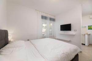a white bedroom with a white bed and a television at Studio apartman Lea in Baška