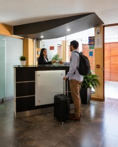 a man with a suitcase standing at a counter with a woman at Mandala Rooms & Services in Arequipa