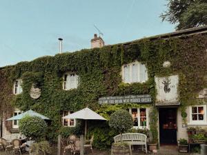 an ivy covered building with chairs and an umbrella at The Roebuck Inn in Mobberley