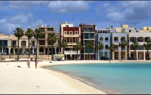 two people walking on the beach in front of buildings at Arzella Beachfront Guesthouse in Birżebbuġa