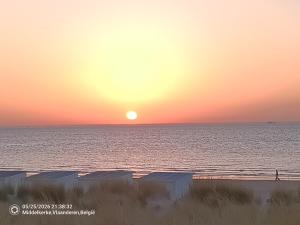 a sunset over the ocean with a person walking on the beach at Art Donna met zeezicht in Middelkerke