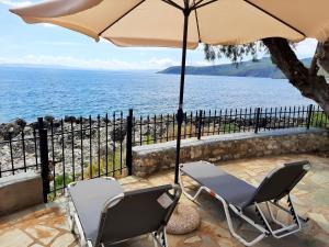 two chairs and an umbrella on a patio next to the water at Seafront Villa, Fay in Kardamyli
