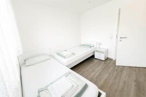 two beds in a room with white walls and wooden floors at STAY - Seeblick Apartment in Friedrichshafen +23 photos