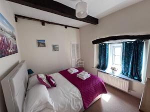 a bedroom with a bed with purple sheets and a window at Eagle Cottage in Penrith