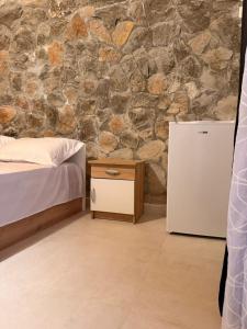 a bedroom with a stone wall with a bed and a refrigerator at Perseku GuestHouse in Shirokë