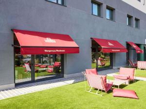 a patio with chairs and red umbrellas in front of a building at Ibis Styles Madrid Airport Valdebebas in Madrid