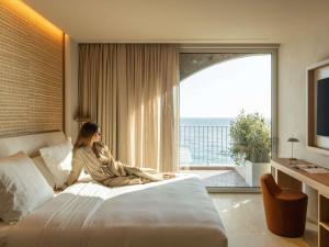 a woman sitting on a bed in a hotel room at Green Coast Hotel MGallery Collection in Vlorë