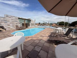 a swimming pool with chairs and a table and an umbrella at Pousada Recifes de Corais in Porto De Galinhas