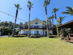 a house with palm trees in front of it at Long Beach Pension in Seogwipo