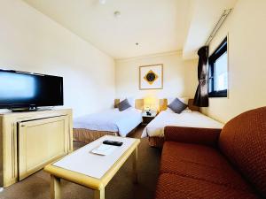 a hotel room with two beds and a couch and a tv at Hotel The Centre Utsunomiya in Utsunomiya