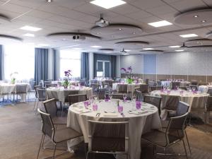 a banquet room with white tables and chairs with purple flowers at Novotel Massy Palaiseau in Palaiseau +104 photos