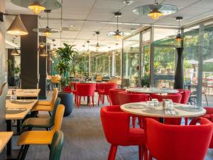 a restaurant with red chairs and tables and windows at Novotel Poissy Orgeval in Orgeval