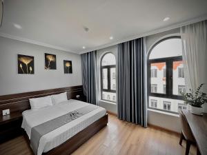 a bedroom with a bed and a desk and two windows at HS Dobry Hotel Ha Long in Ha Long